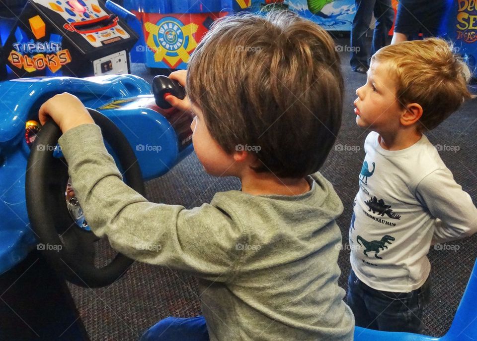 Little Boys At A Videogame Arcade. Young Boys Playing A Shooter Videogame
