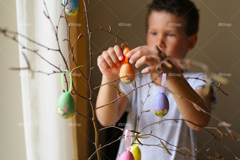 a boy of seven years old, paints crafts at home, Easter eggs, the boy is preparing for the holiday. home crafts, craft activity. a child decorates a tree branch with homemade eggs for Easter