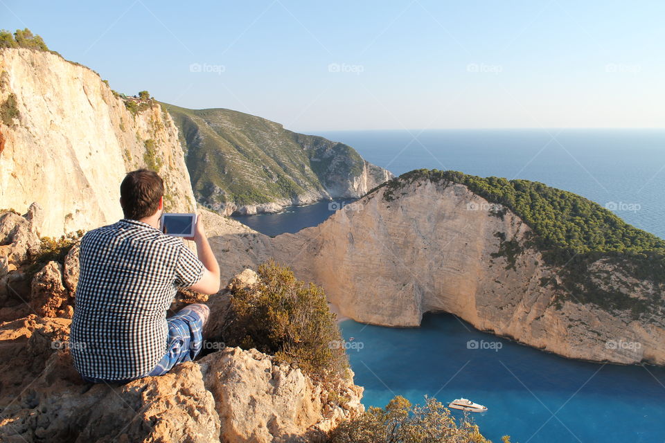 Man sitting on a cliff and taking  photograph