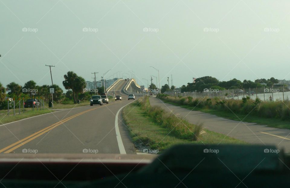 Road trip going towards the beach in central eastern Florida by the Atlantic Ocean meeting some cars on the opposite side of the road, by a curved and nice high bridge with street lights.