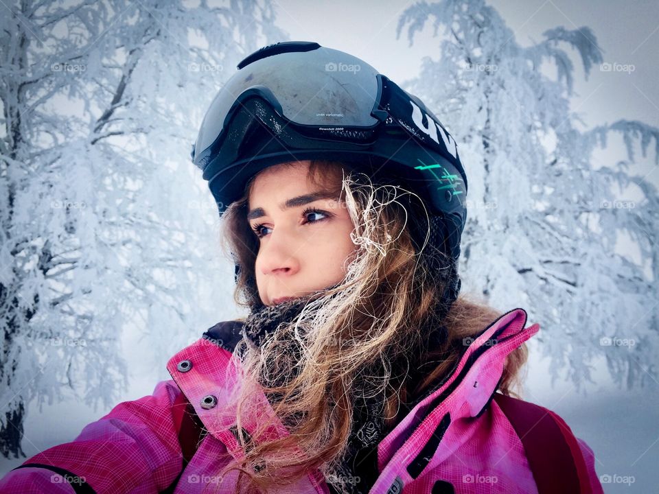 Portrait of woman with frozen hair and Uvex ski glasses surrounded by trees covered in snow