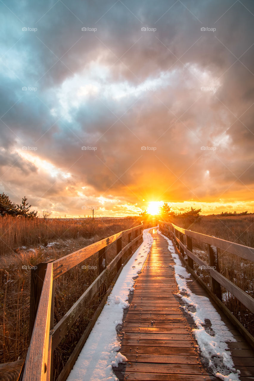 Boardwalk leading off into the sunset, as dark storm clouds create a moody dramatic scene. 
