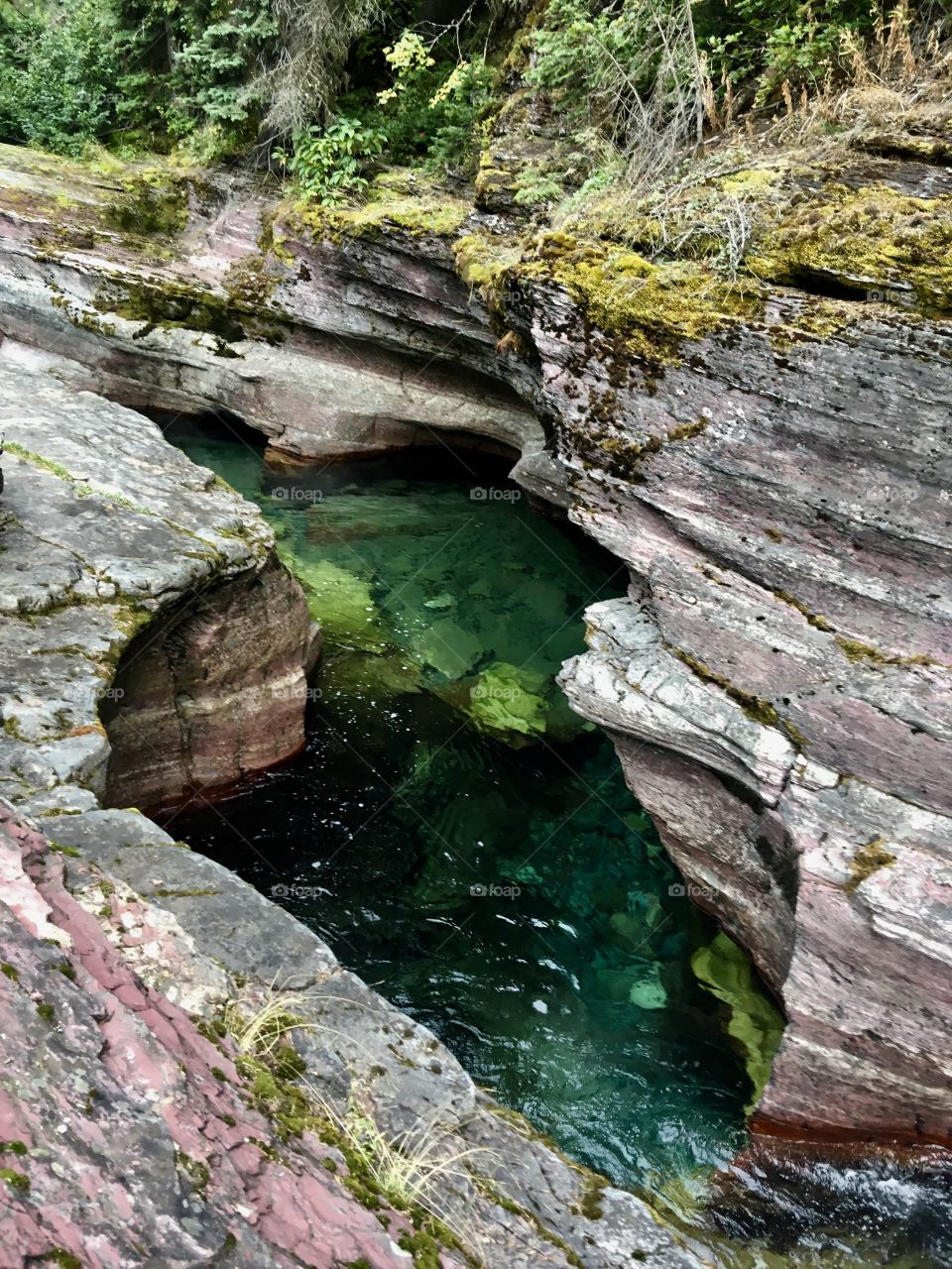 Photo shot in glacier national park in Montana. The water between the two rocks created a gorgeous stream. The water paved its way through the mountain. The color of the rocks gave the water a beautiful green color. 