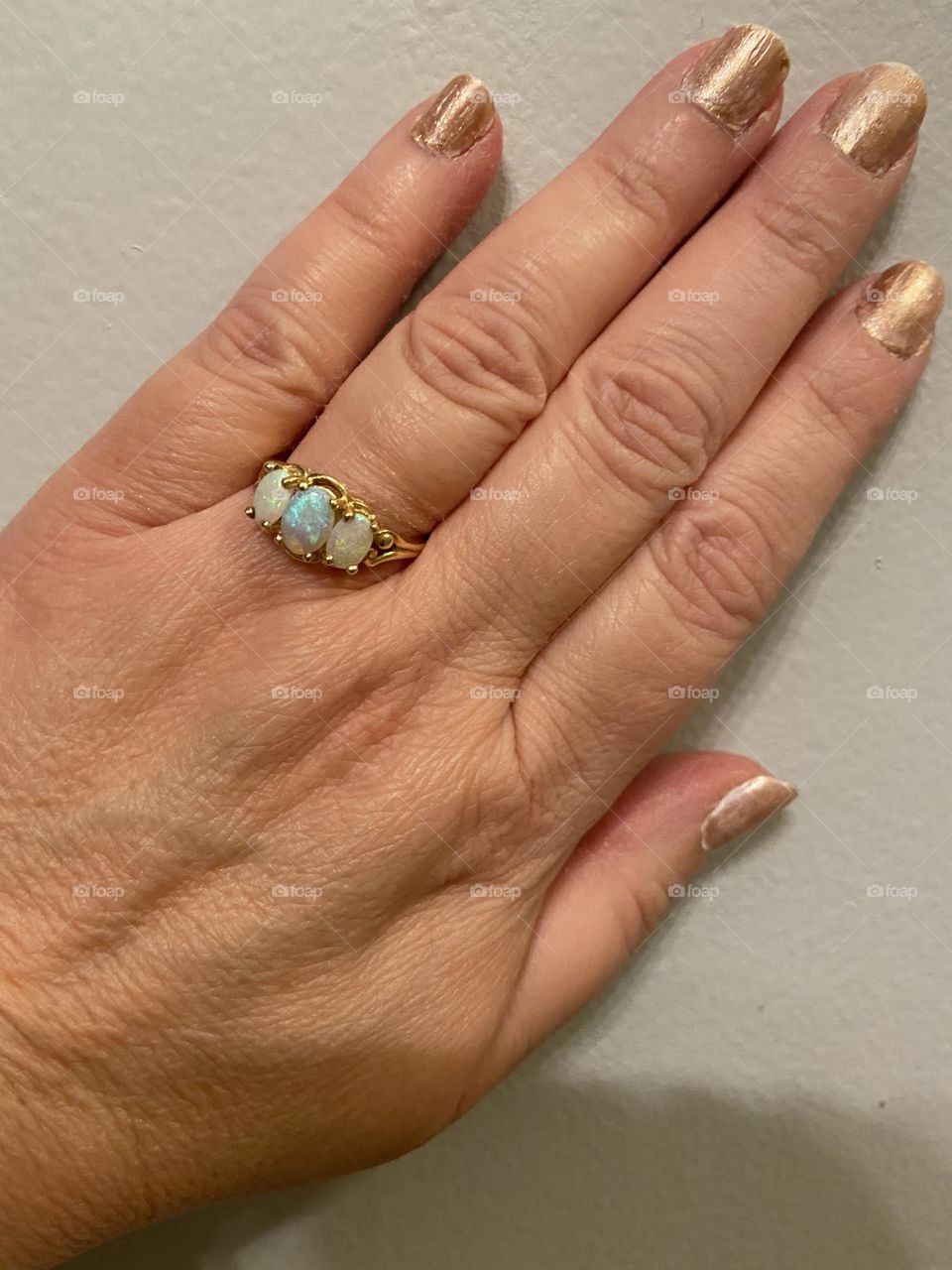 My hand with fingernails painted with a gold-toned polish, which was a base of white with sparkly gold on top. I am wearing an Opal birthstone ring given to me by my late Aunt Helen, who, like me, had an October birthday.