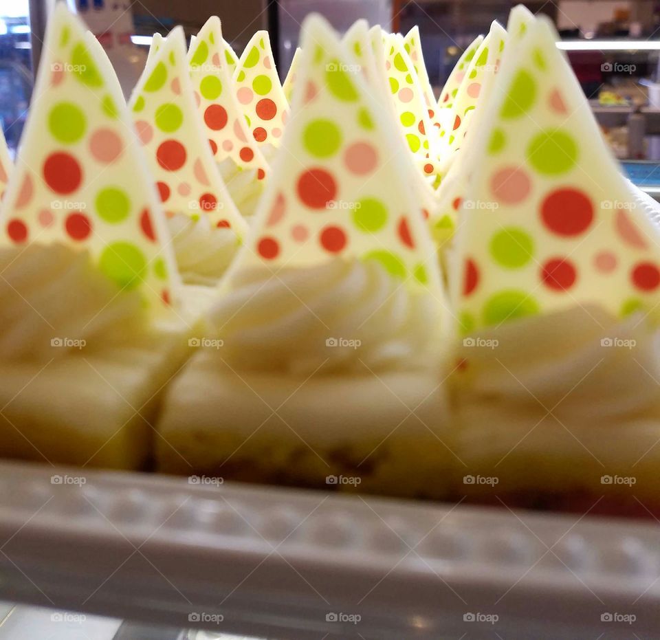 cake with yellow  whipped cream icing ,topped with white whipped cream and a colorful polka dots on white chocolate triangle