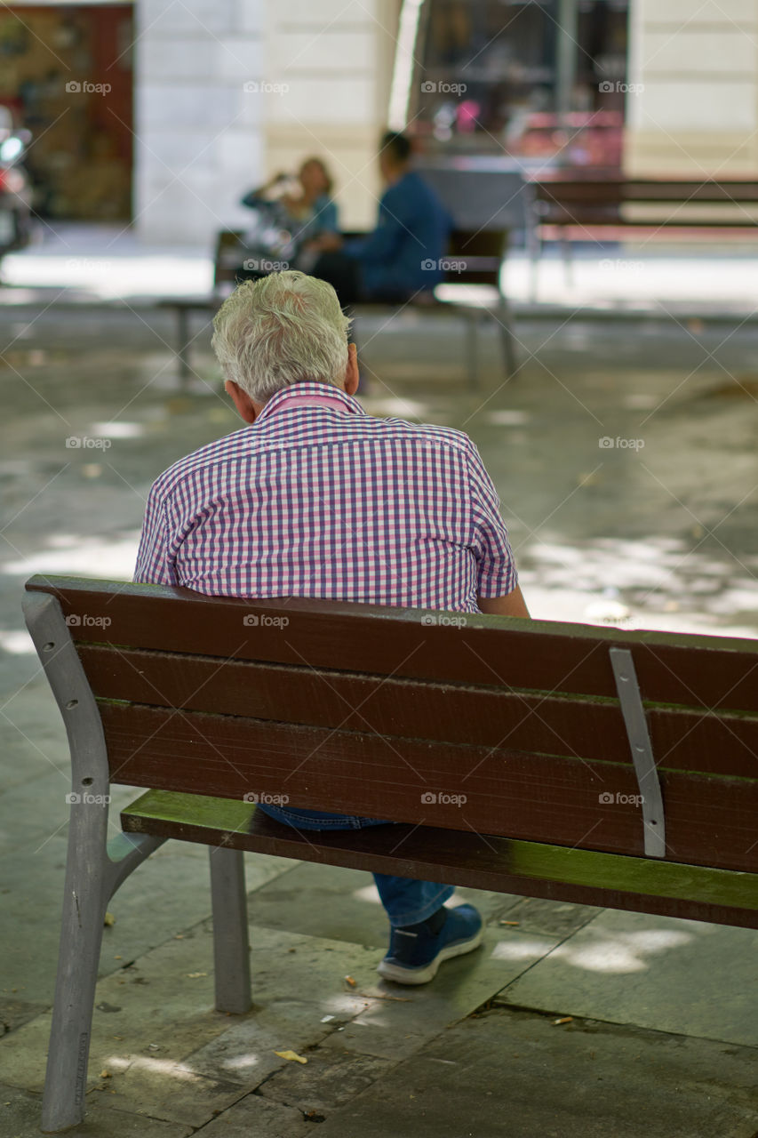 Elderly man sitting in a street bench