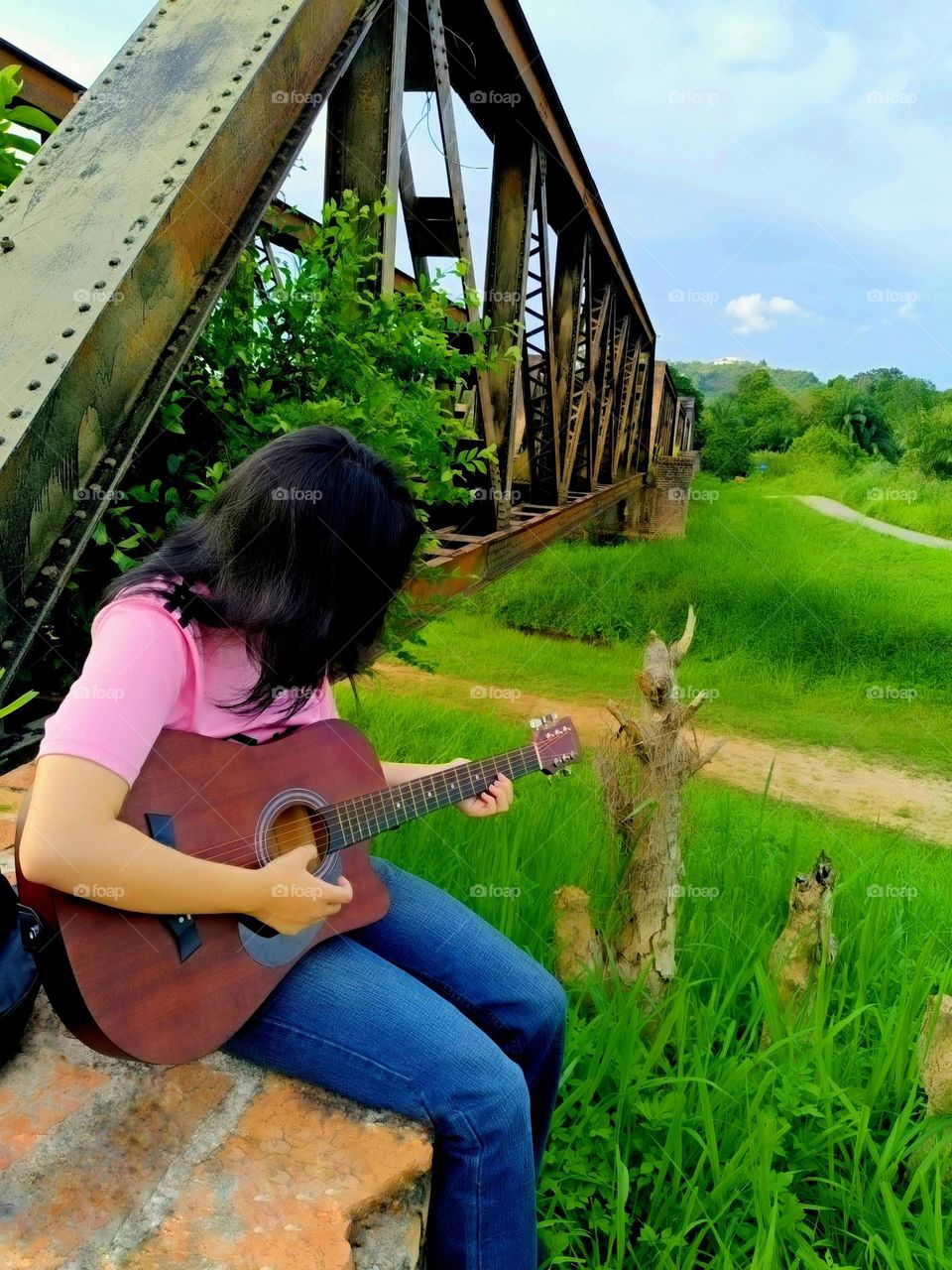 A Chinese girl was playing the guitar near the old iron railway bridge.