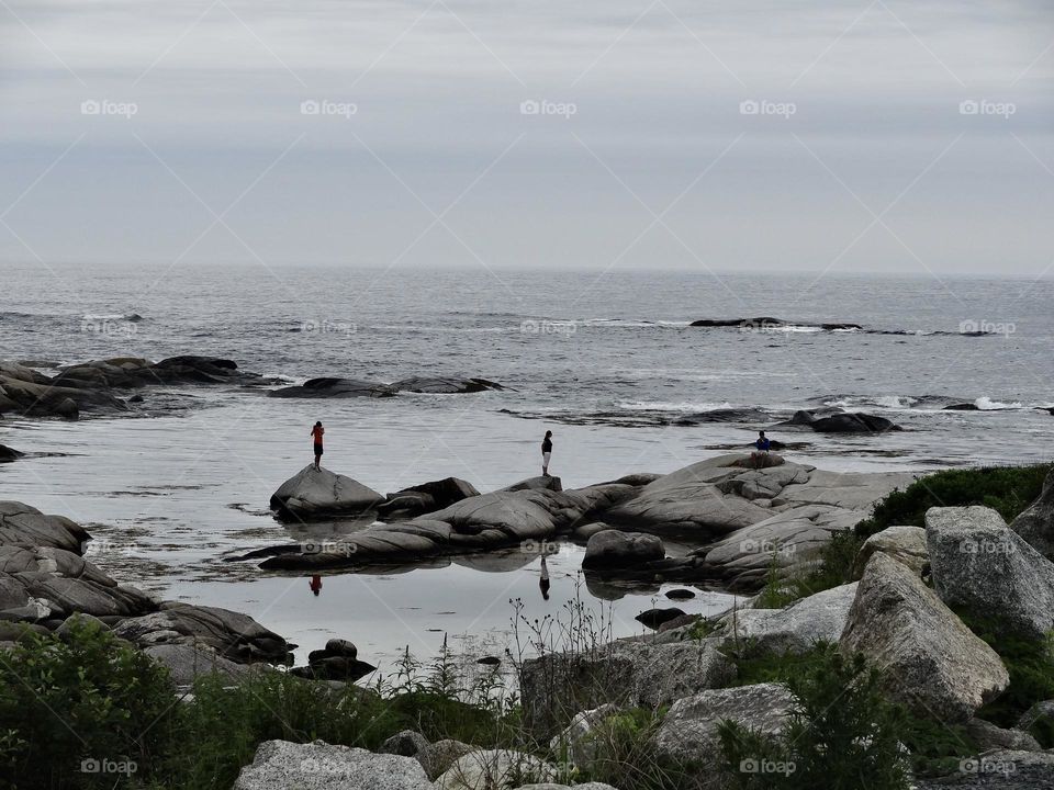 Rocks and water view at peggys cove two people standing on the rocks surrounded by water , cloudy day 