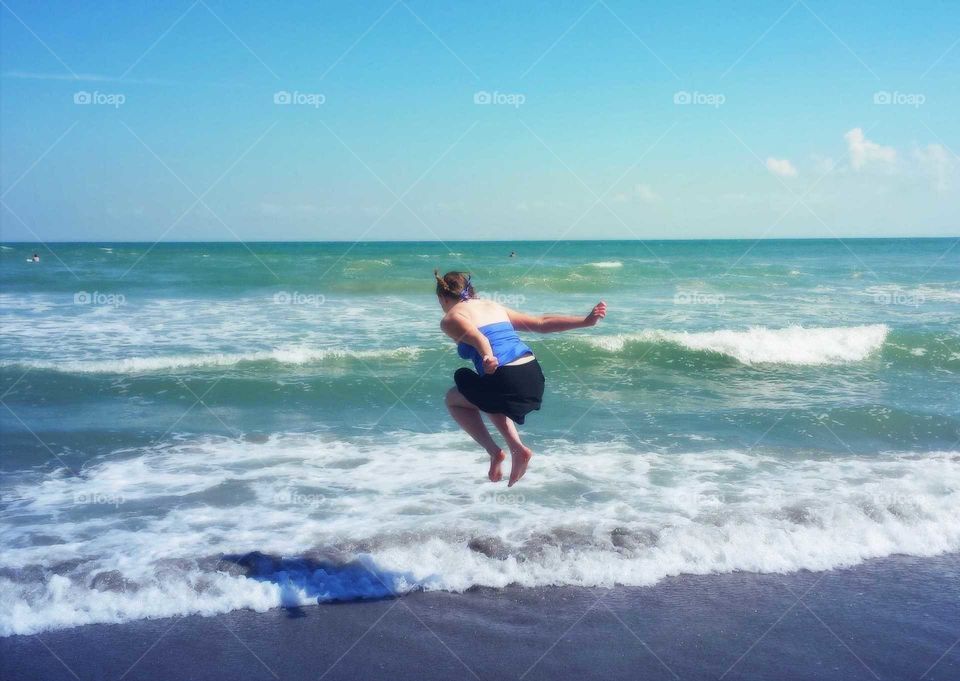 Girl jumping over waves on hot summer day.