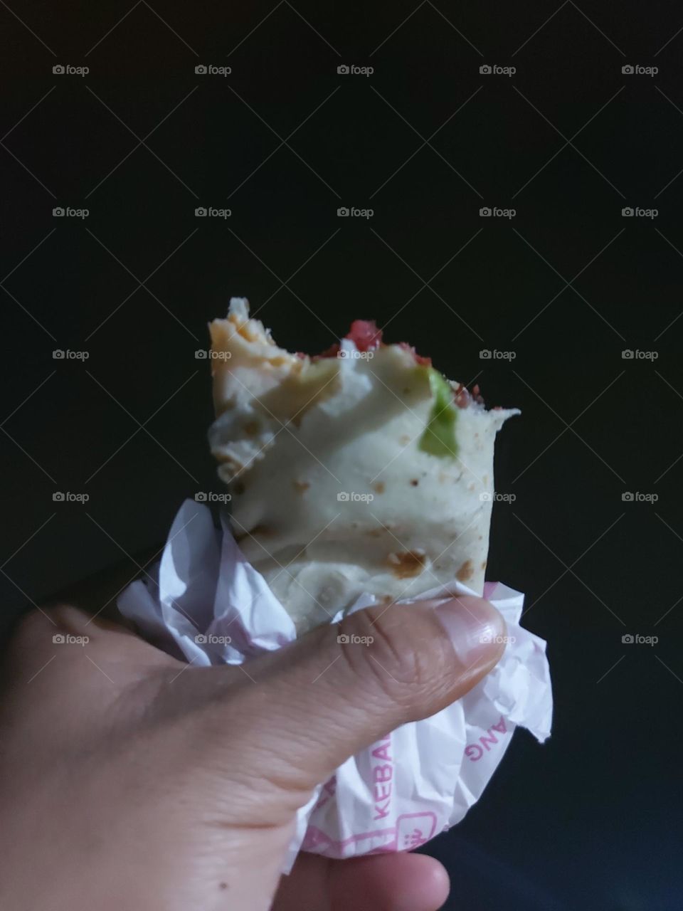 A man's hand shows a partially bitten kebab dish against the background of the night sky