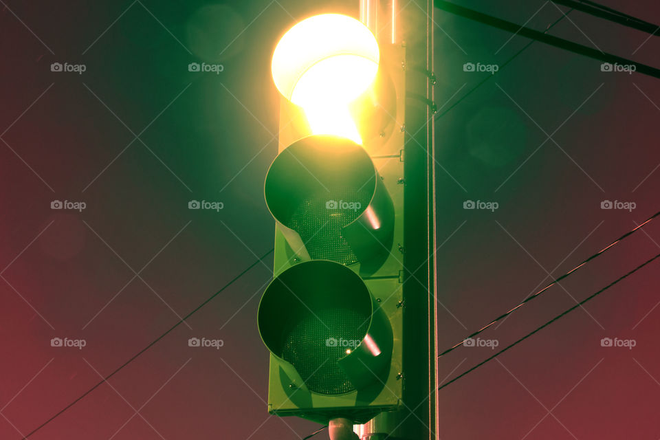 A timelapse exposure of a traffic light at late hours of the night leaves glowing hot yellow against a burgundy night sky.