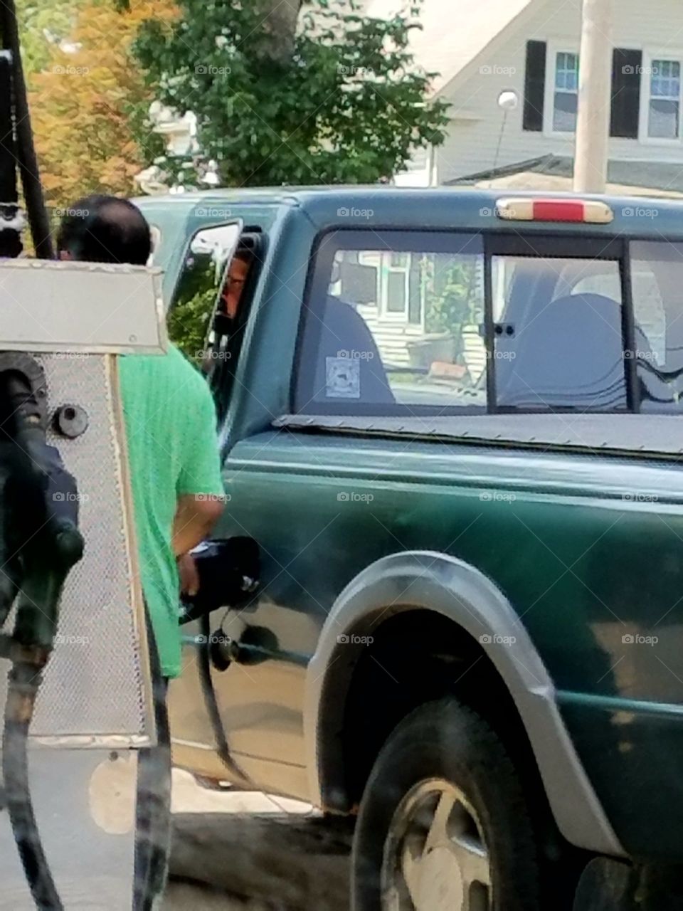 Gas station, paying attendant through window of green pickup.
