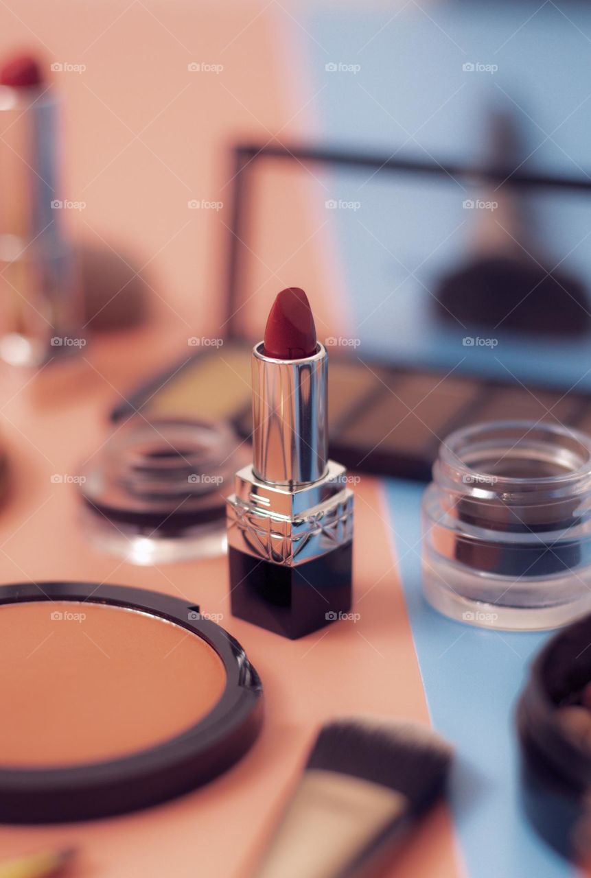 Red lipstick among the blurred makeup cosmetics set stands on a blue-pink background, close-up side view. The concept of female cosmetics, beauty salon.