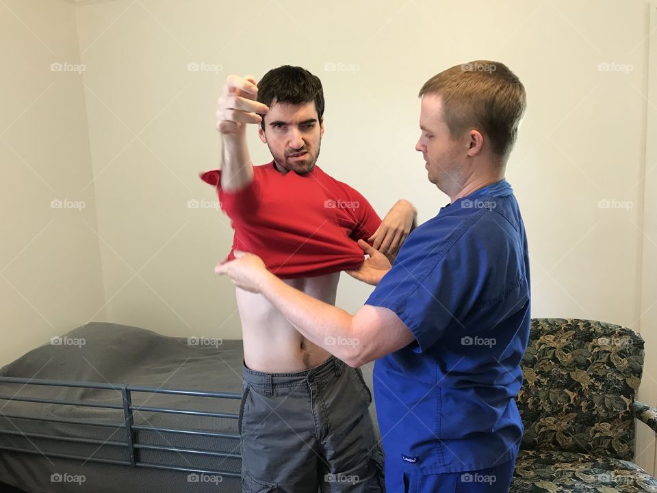 Aide helps patient put his shirt on.