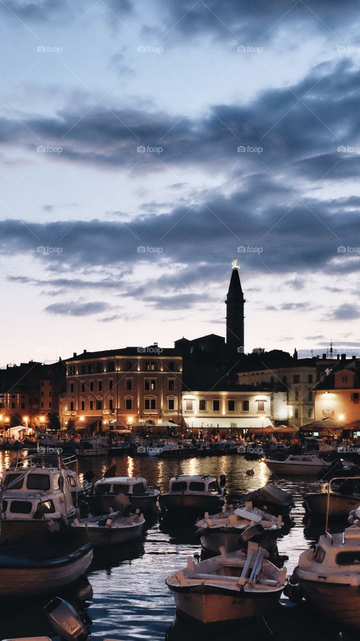 Rovinj, Croatia, and the tower of the church of St Euphemia silhouetted at sunset behind moored boats in the harbour.