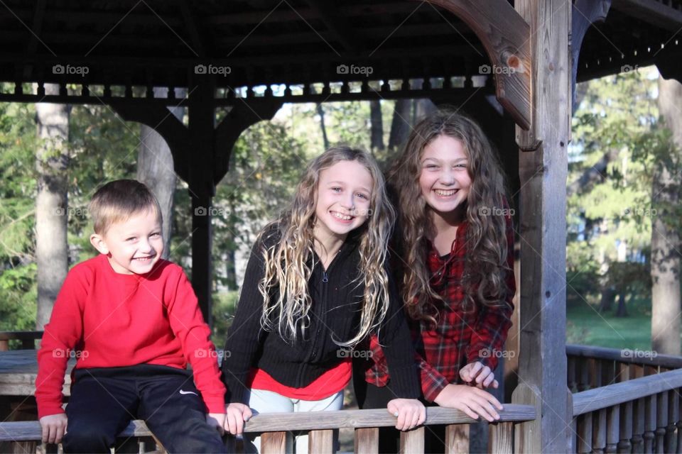 Three giggly siblings enjoying a warm Autumn day under a wooden gazebo. 