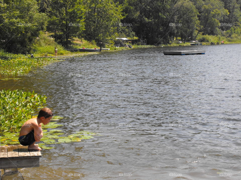 Young boy crouched down at the end of a lake pier