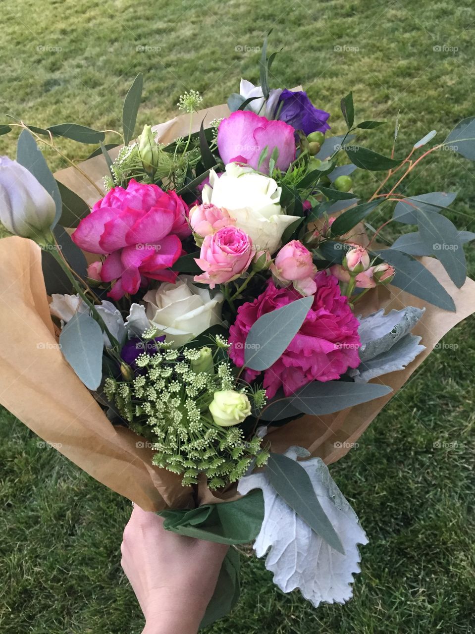 Beautiful, lush pink, purple, white and green bouquet of flowers with carnations, roses, and peonies being held in a woman’s hand