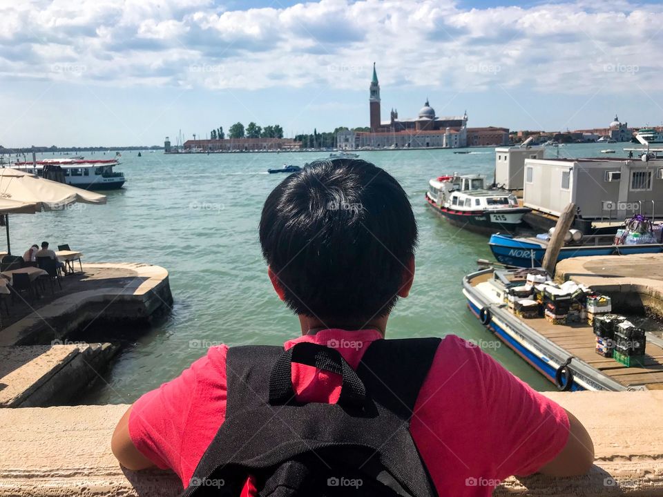 A boy on red shirt wearing a black backpack was standing and looking at the palace from far away,scenery so wonderful 