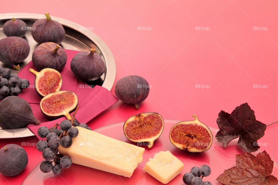 Figs, black grapes and aged cheese on a bright background.