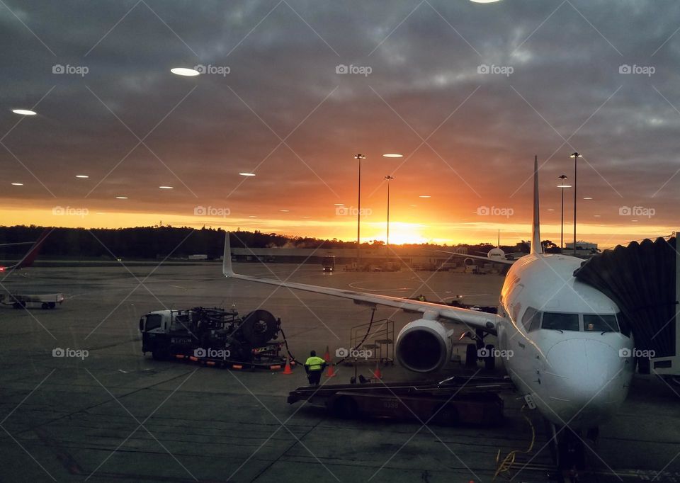 A sunrise illuminates the side of a plane on a cloudy morning