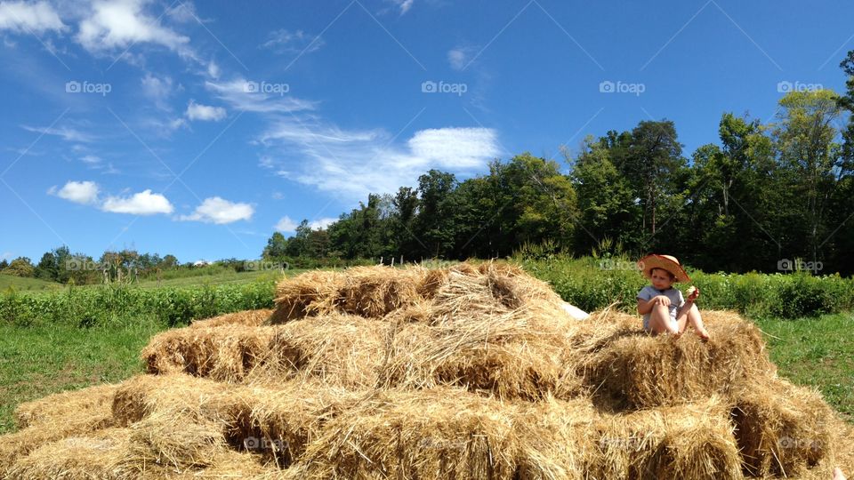 Kid sitting on a haystack in the sun. Panoramic.
