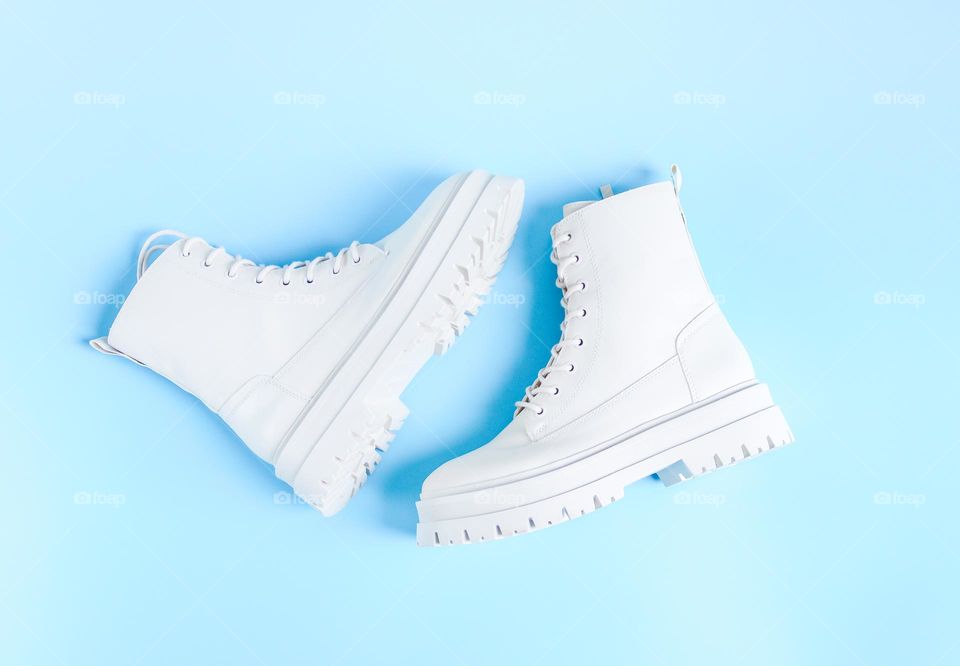 One pair of beautiful white Martens brand shoes on a rough tractor sole with lacing lie in the center on a light blue background,flats Lay. The concept of fashionable women's shoes.