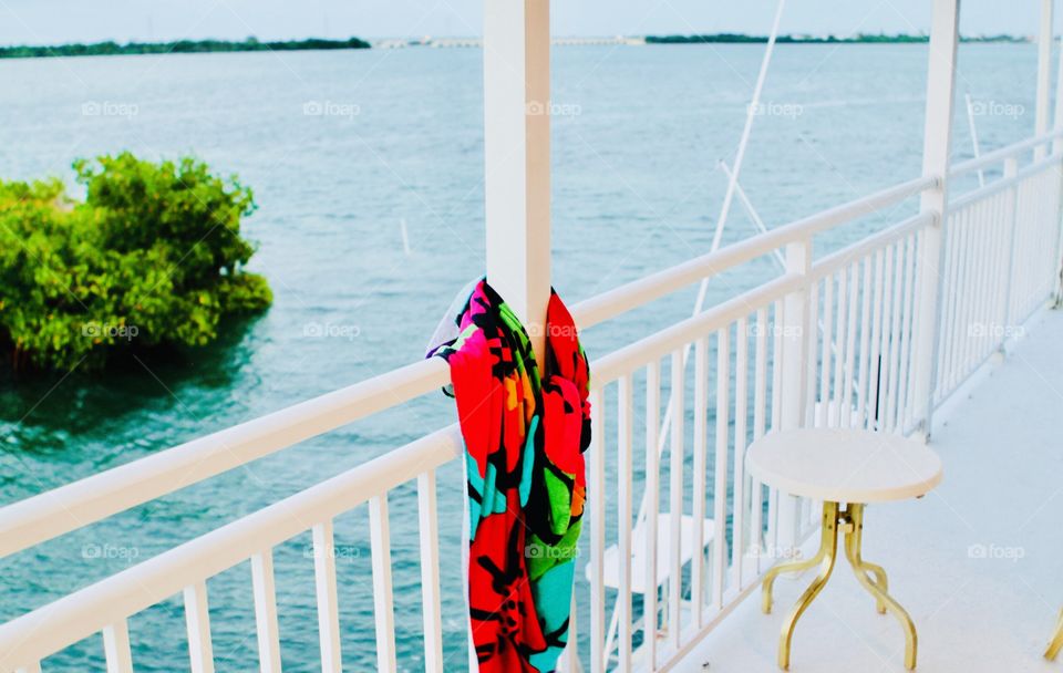 Gorgeous brightly colored beach towel hanging looped around white deck post with ocean in the background. 