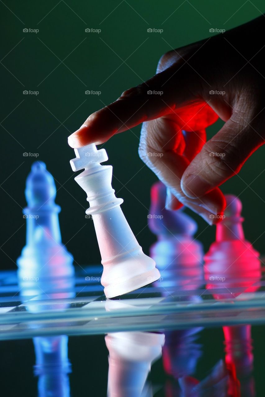 finger tilting a chess piece on a glass chess board