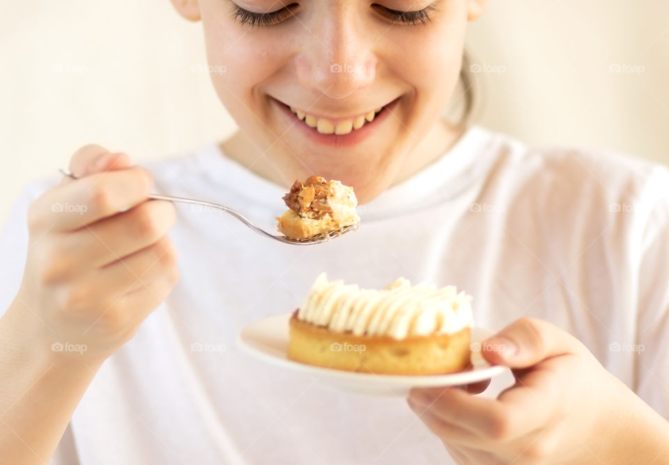 Child smiling and eating a delicious vanilla cake with cream and nuts.