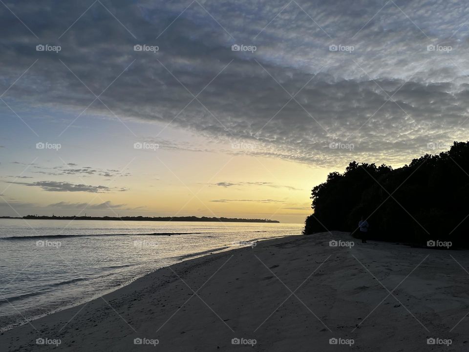 An elegant sunrise at Thaa atoll Veymandoo island. The sun shining behind the island draws a beautiful pattern in the horizon through the island line and clouds up in the sky.