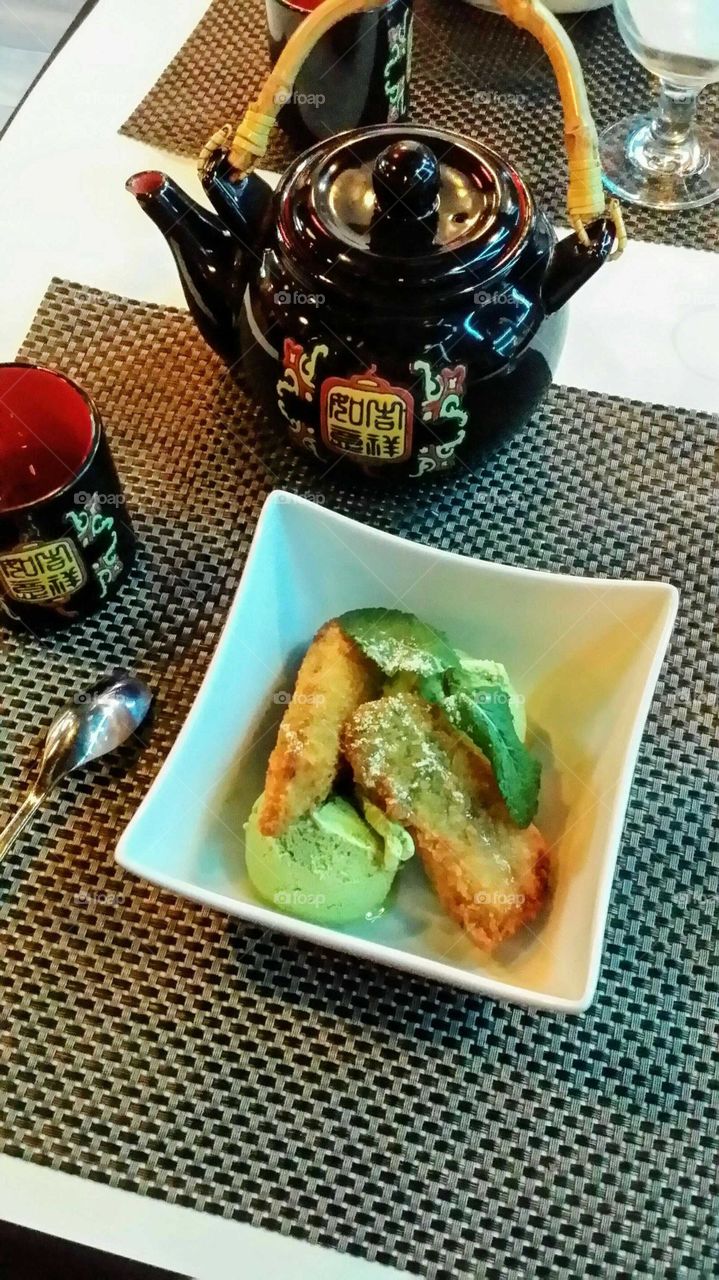 Fried bananas,  green tea ice cream and a mint leaf  with a tea pot and a cup