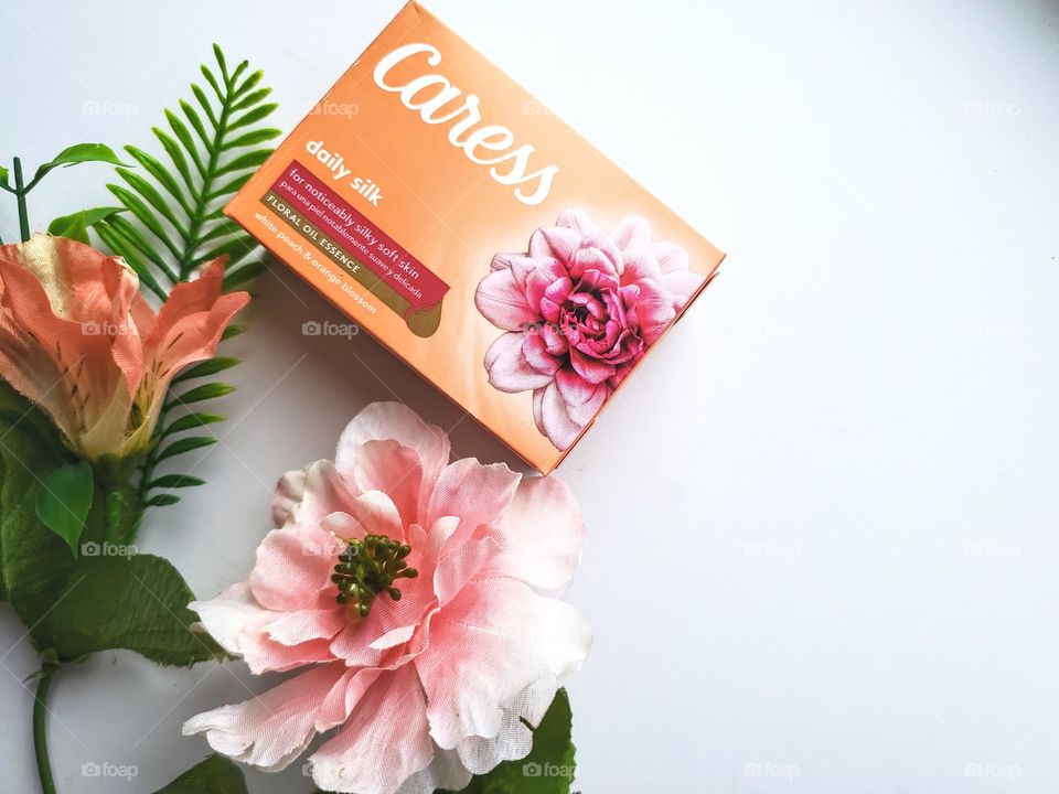 Left side oriented :  The new Caress soap bar daily silk next to matching florals on a white background.