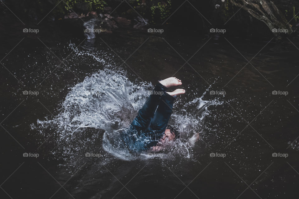 A boy having fun by jumping into the stream, making the splashing water around him