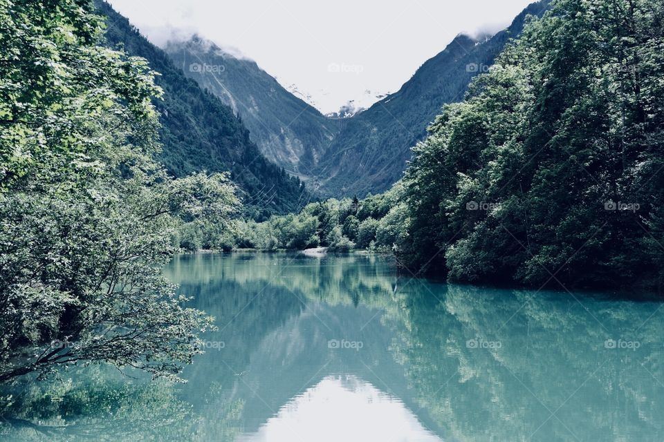 A lake between cloudy mountains with some Green trees