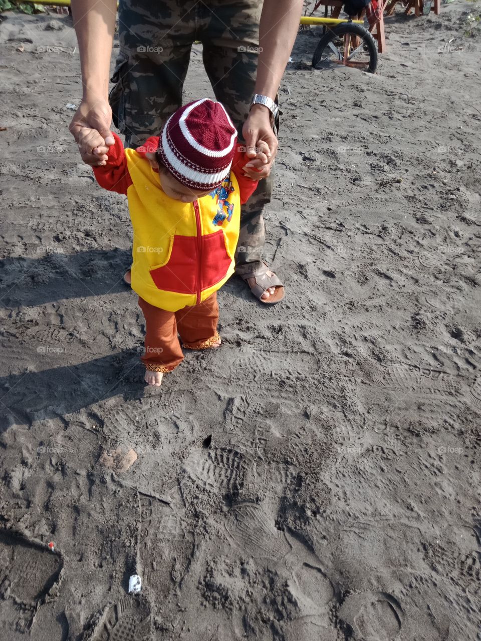 a baby boy learns to walk with his father on the beach