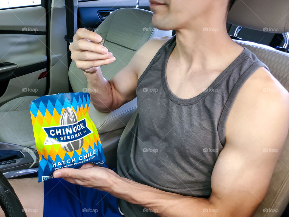 Favorite road trip snacks- Closeup of a fit man in his car with eating Chinook sunflower seeds.