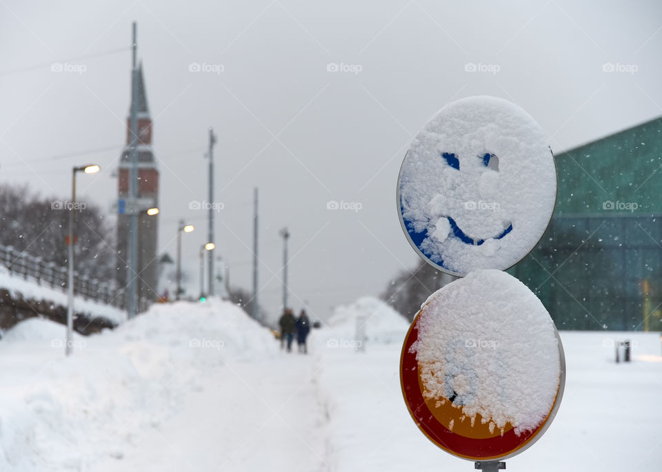 Snowy traffic sign with a smiling face drawn into snow in the center of Helsinki, Finland.