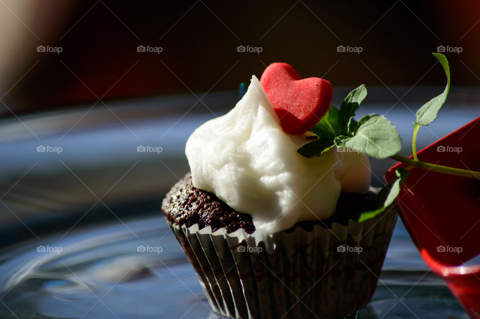 Dreamlike chocolate cupcake with red candy heart on vanilla buttercream and mint leaf arrow shining in golden hour sunlight beautiful artisanal food photography background