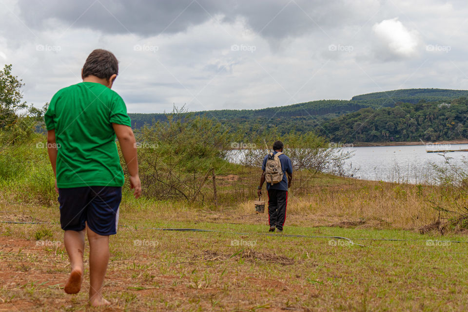 Criança e adulto caminhando em direção a represa para pescar.