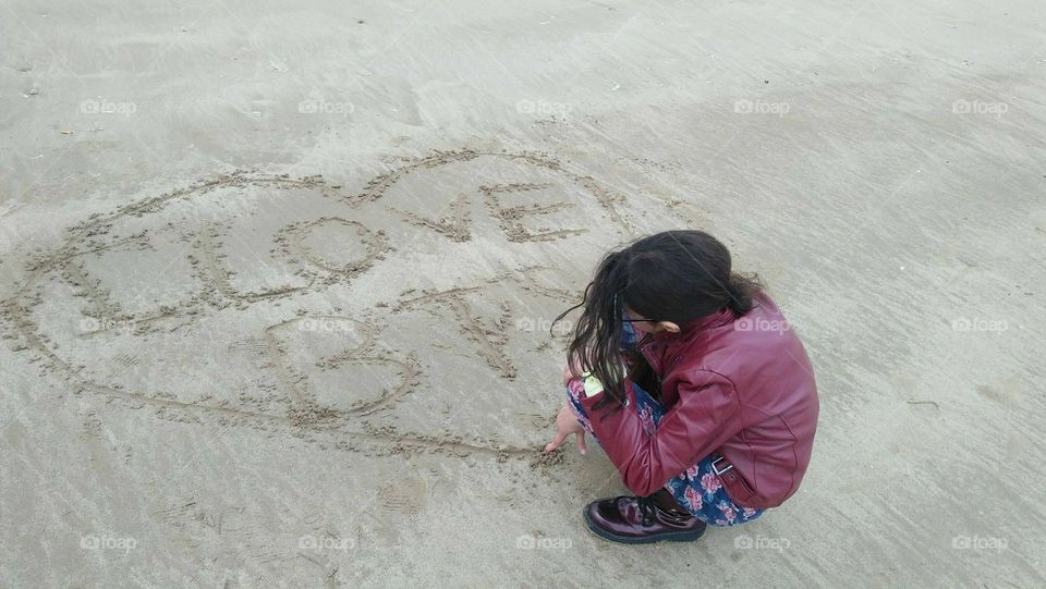 A young girl draws on sand