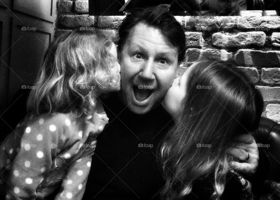 Close-up of daughters kissing their father on cheek