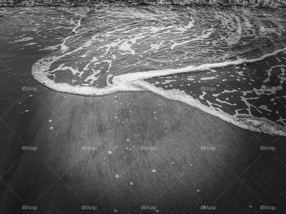 Texture and background of soft wave foam on sandy beach in black and white
