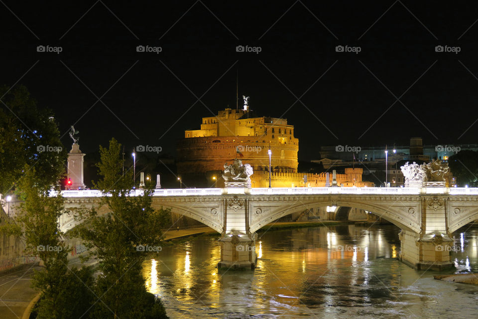 Rome a bridge on Tiber river before Castel SantAngelo at night. Ponte SantAngelo castle visible in the background at Rome Italy.