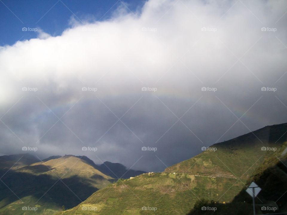 Faint rainbow and cumulus clouds casting shadows over the vast mountains of Ecuador 