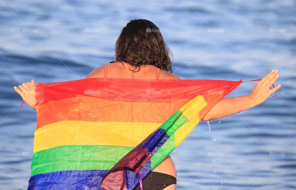 Young woman from behind holding a gay flag 