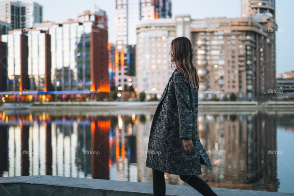 Young woman walking on street near city river at night 