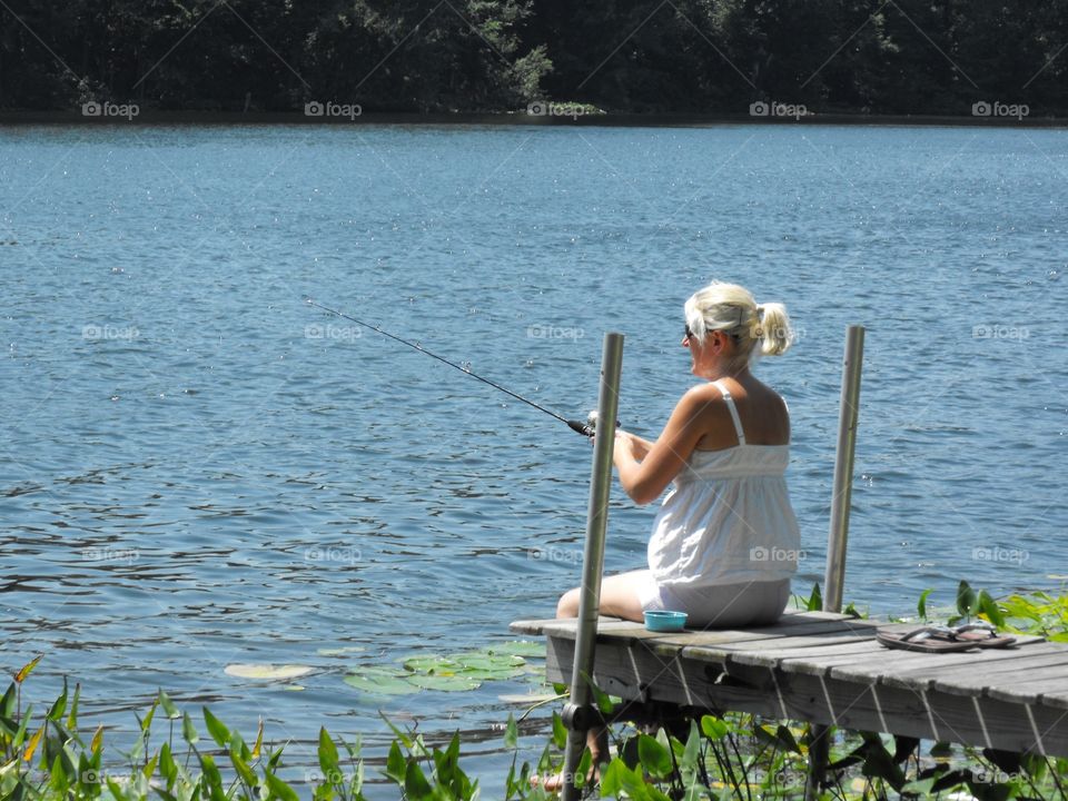 Woman fishing off a pier at a lake.