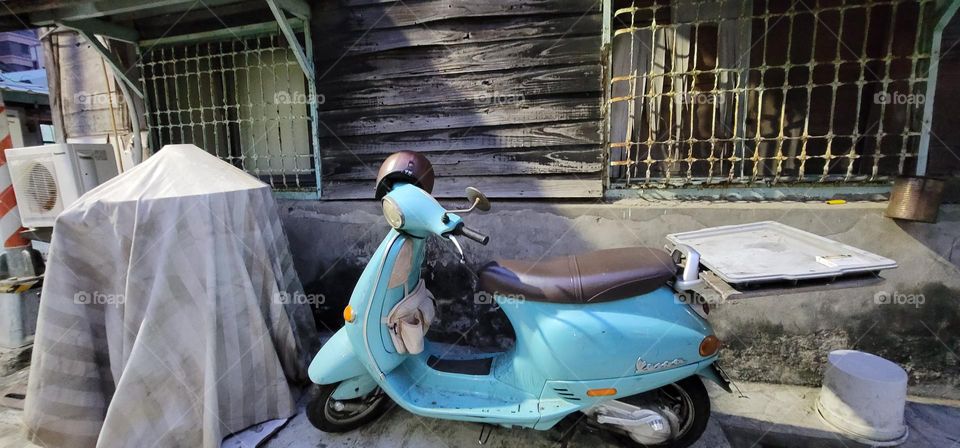 A water blue motorcycle parked outside a wooden house