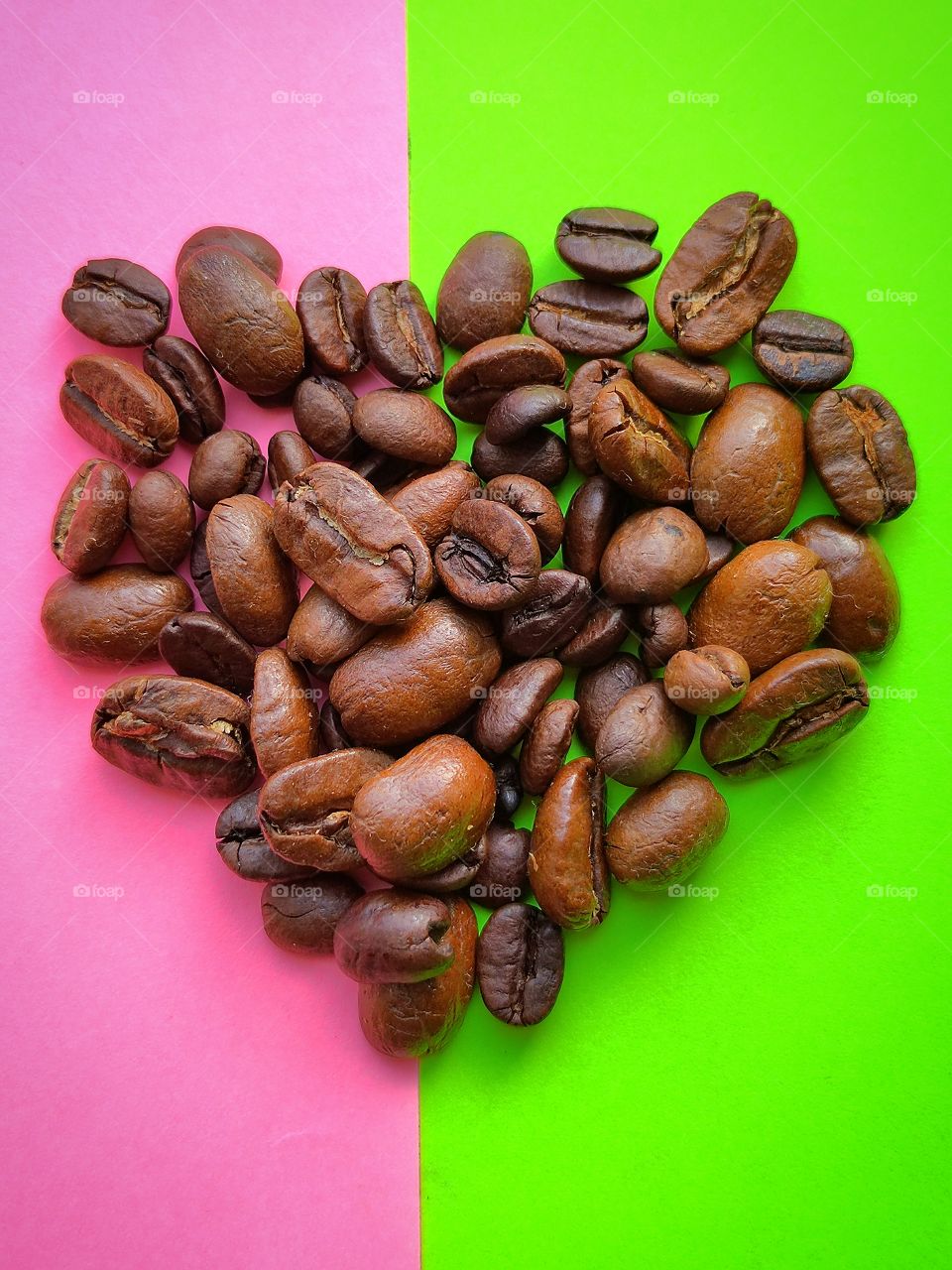 Roasted heart shaped coffee beans on pink and light green backgrounds.  Color contrast